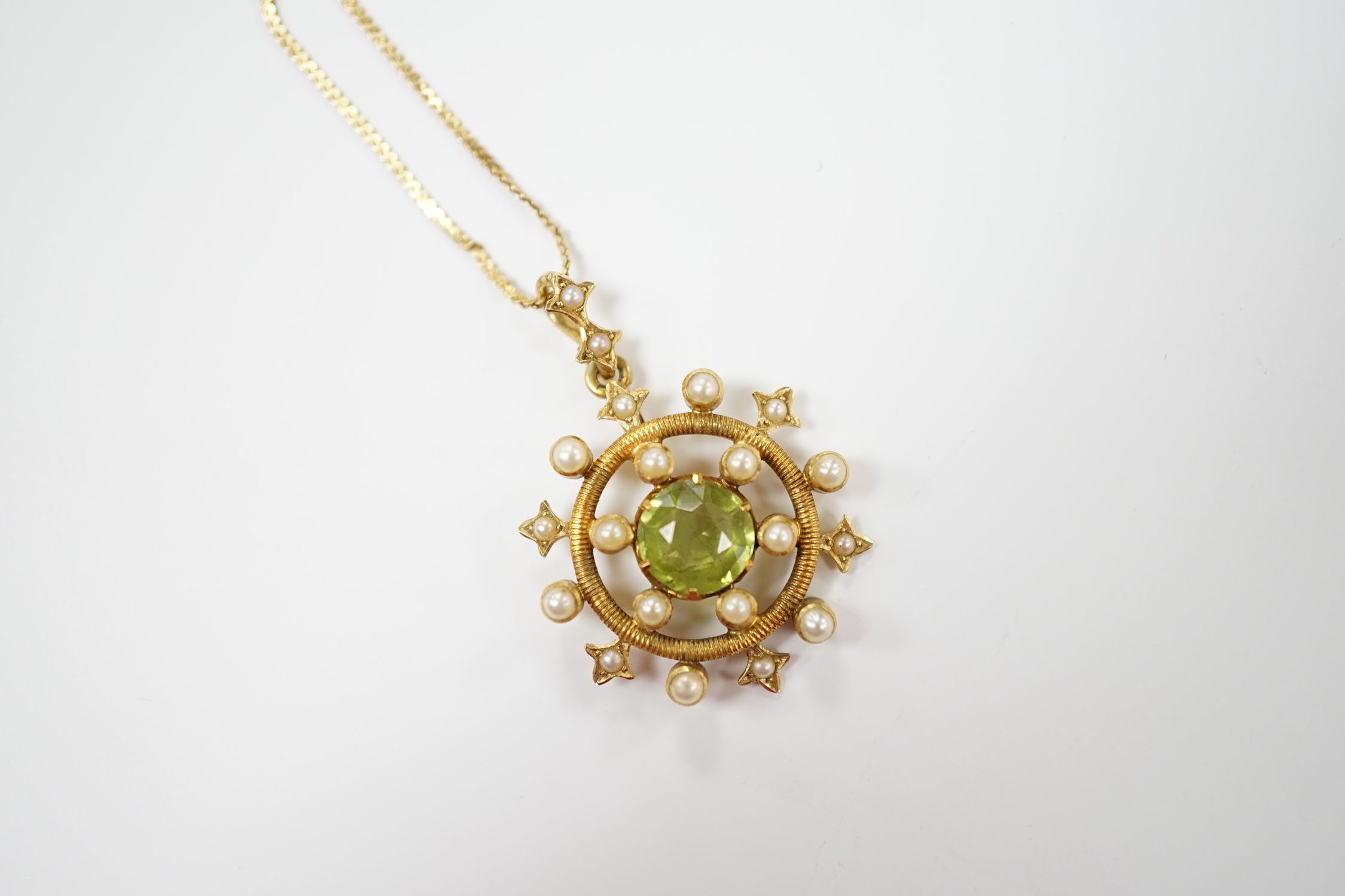 An Edwardian yellow metal, peridot and seed pearl cluster set 'wheel' pendant, overall 30mm, on a later 14k chain, gross weight 5.2 grams.